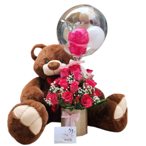 Cilindro con 24 rosas fucsias, decorado con follaje perla y cafeto, acompañado de un globo burbuja personalizado y un peluche de 70 cm